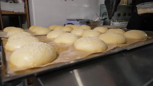 Closeup of the Chef Sprinkling Sesame Seeds on Round Burger Buns Before Baking