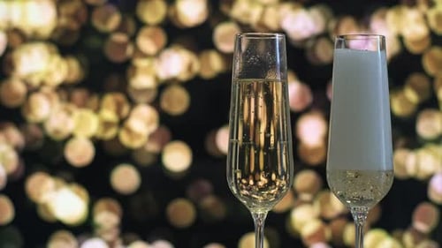 Dos copas de champán, una llena de vino espumoso, sobre un fondo de bokeh dorado l