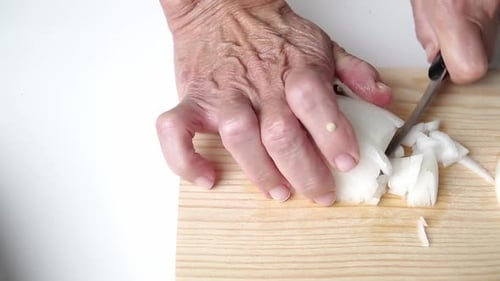 Caucasian person with old hands, cutting onion, on a wooden board. Cenital shot of food from above.