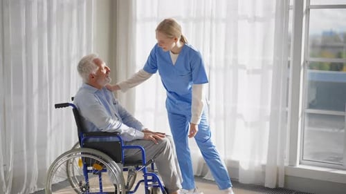Nurse Comforting Elderly Man in Wheelchair, Bright Room