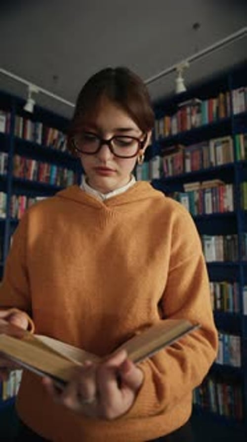 Female Student Reading Book in Library in front of Bookshelf