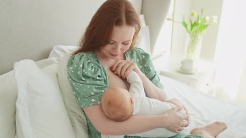 Mother Breastfeeding Infant on Bed in Bright Room