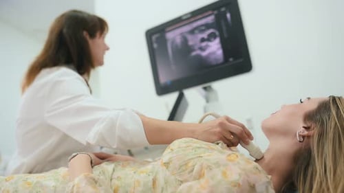Woman is lying down and undergoing ultrasonic test of the thyroid gland.