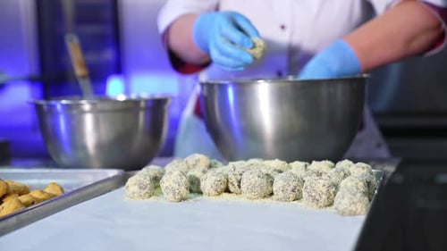 Sweet desserts in a shape of balls are laid on the tray. Worker covers the biscuits with crumbles.