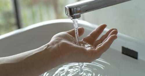Water Flowing from Faucet onto Hand in Bathroom