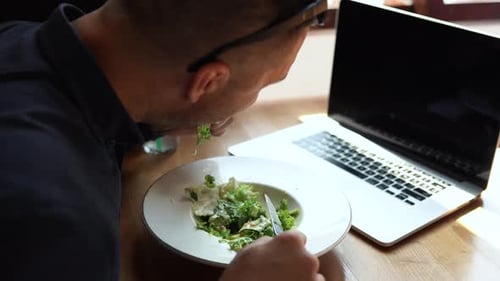 a Man is Eating and Working on a Laptop in a Restaurant
