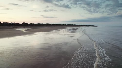 Von oben zeigen Luftaufnahmen einen faszinierenden Strand bei Sonnenuntergang mit schimmerndem, nassem Sand, ein Meer