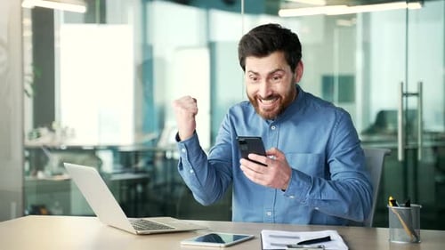 Shocked surprised handsome businessman received great news on phone sitting in business office