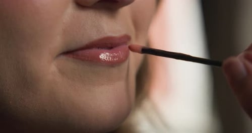 Seitliche Zeitlupenansicht der weiblichen Lippe mit Visagistin, die während ihres We Lipgloss auf ihre Lippen aufträgt