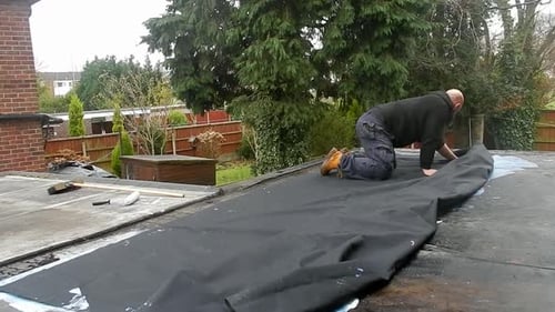 Man Installing Roofing Material on Flat Suburban Roof