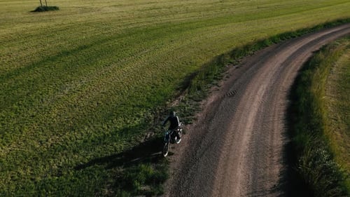Biker on dirt road, gets on bike and drives away between the fields