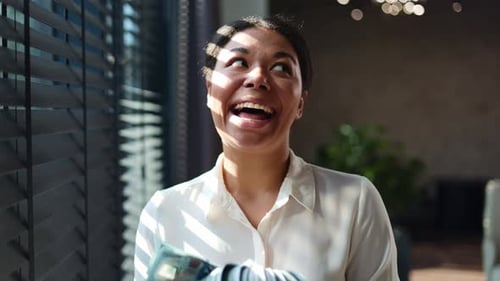 Female Entrepreneur Holding Fan of Dollar Banknotes and Dancing at Office