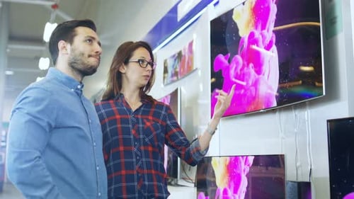 Young Couple Shopping for a New 4K TV Set in the Electronics Store. They're Trying to Decide on the