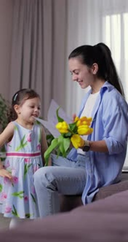 Young Girl Gives Flowers to Smiling Woman at Home