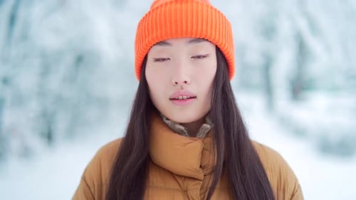 beauty portrait of young asian woman standing on snow background in park in cold weather and looking