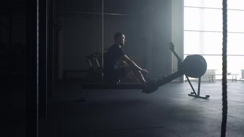 Athletic Man Doing Exercise In Gym Using Rowing Machine For Developing Power Of Arms
