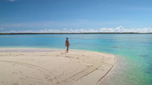 Young Woman Walking on a White Sand Beach Towards a Turquoise Lagoon in Maupiti French Polynesia