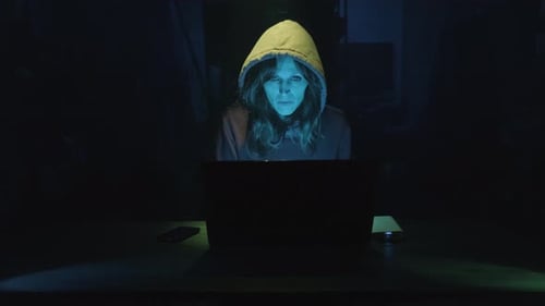 Woman in Hoodie Using Laptop in the Dark