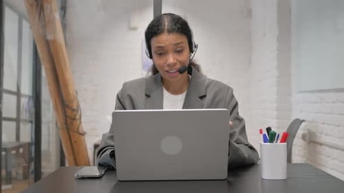 African American Businesswoman with Headset in Call Center Doing Video Chat via Laptop