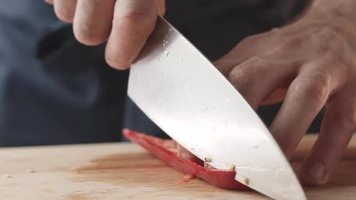 View of the Young Chef Cut Thin Slices of a Piece of Red Pepper with a Knife