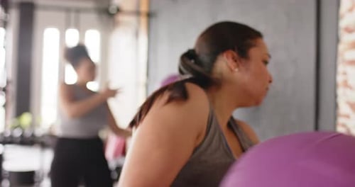 Gripping purple medicine ball, woman propelling ball toward brick wall at gym feeling rebound force