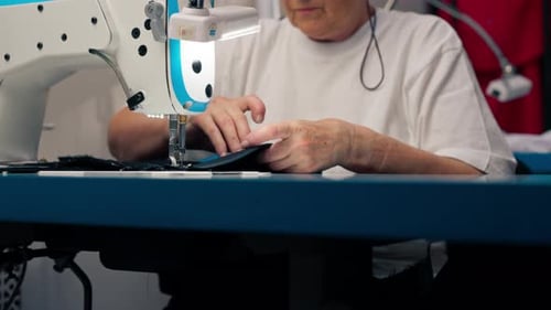 Gros plan dans un atelier de couture sur une machine, le vieux maître couturier fait une coupe sur un tissu noir