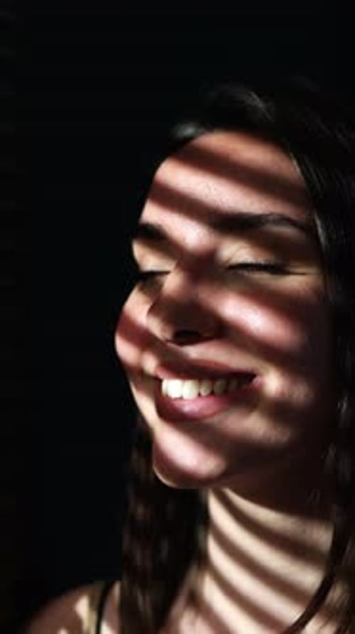 Belle jeune femme souriante à travers les stores de fenêtre, motif d'ombre et de lumière