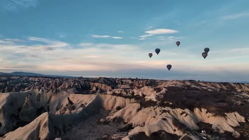 Cinematic drone view low over Cappadocia rocks with numerous floating hot air balloons