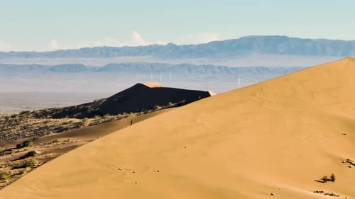 Large sand dune with wind turbines and mountains in the distance