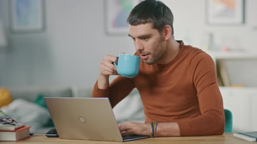 Man Works on Laptop, Sips Coffee at Desk