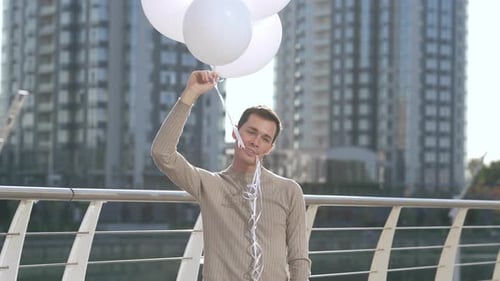 Young Adult Holding Balloons Near a City Bridge