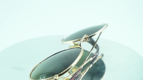 Eine Nahaufnahme einer goldenen Sonnenbrille auf einem um 360 Grad drehbaren Ständer, Studiolicht, 4K-Produktvideo,