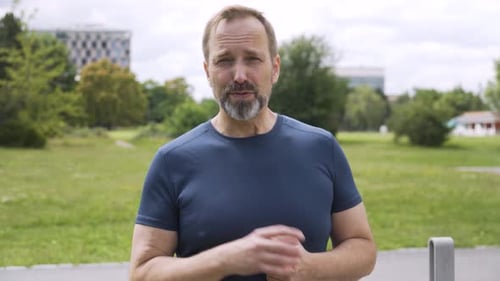 A Handsome Middleaged Caucasian Man Talks to the Camera with a Smile in a Park Closeup