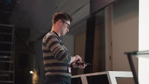 Man Wearing Striped Sweater and Glasses Adjusts Wireless Audio Transmitter on Video Production Set