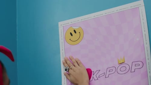 Woman Smoothing K-Pop Style Poster Against Blue Wall