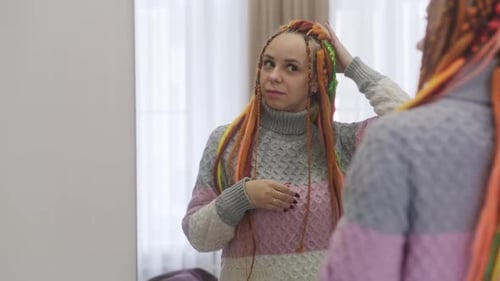 Eine schöne Frau in Freizeitkleidung und mit Dreadlocks schaut in den Spiegel stehend in einem modernen