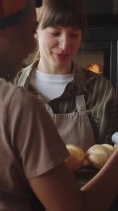 Two Female Bakery Workers Smiling and Talking while Placing Bread on Shelves