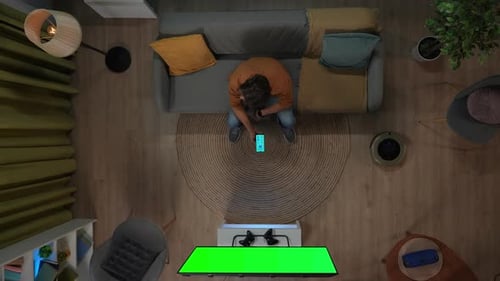 Top View of Man Sitting on the Couch and Switching on House Gadgets Using App on Smartphone Tv with