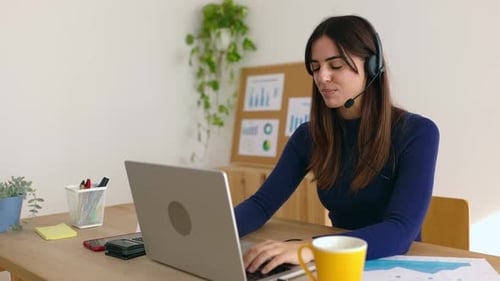 Businesswoman Wearing Headset Working on Laptop Making Video Call From Office