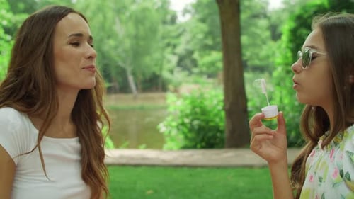 Portrait of Happy Mother and Daughter Playing with Soap Bubbles in Park