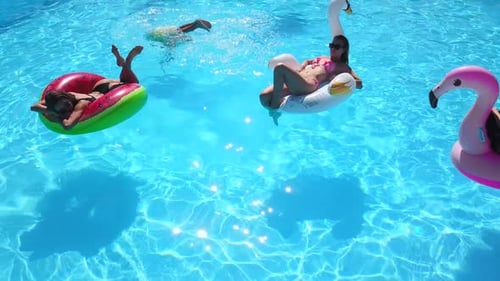People Relaxing on Inflatables in Bright Swimming Pool