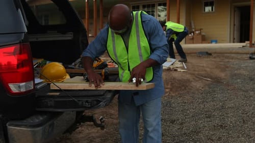 Construction Worker Measures Wood at Job Site With Partner