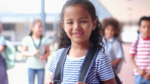 Smiling girl with backpack in school hallway, standing with classmates