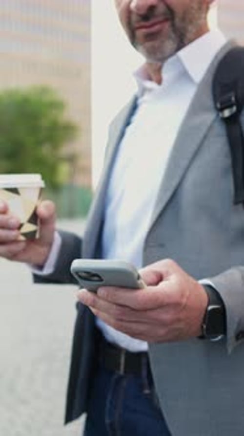 Man Uses Smartphone, Drinks Coffee in City