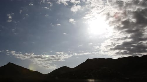 Timelapse of clouds rolling over a mountain range during midday sunlight as the sun moves across the