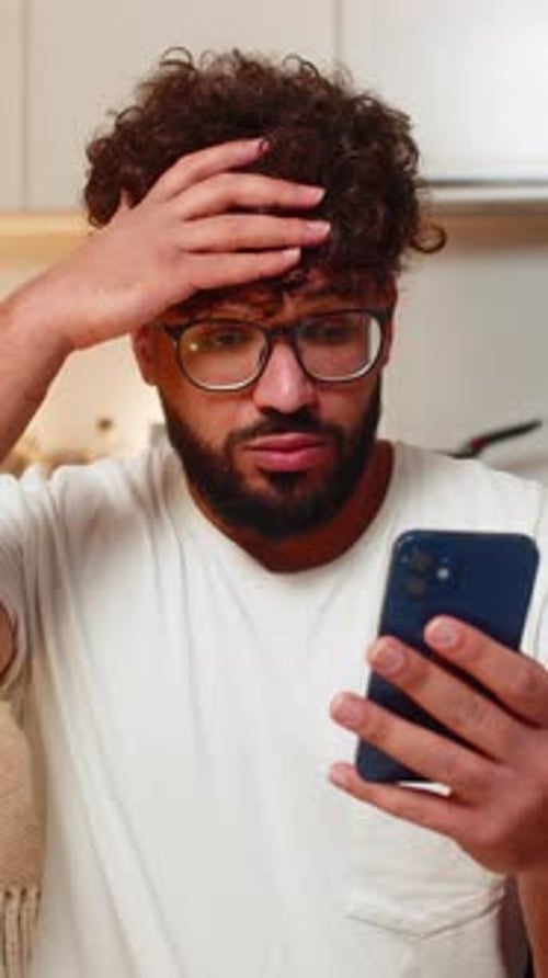 Man Looks at Phone with Confused Expression Indoors