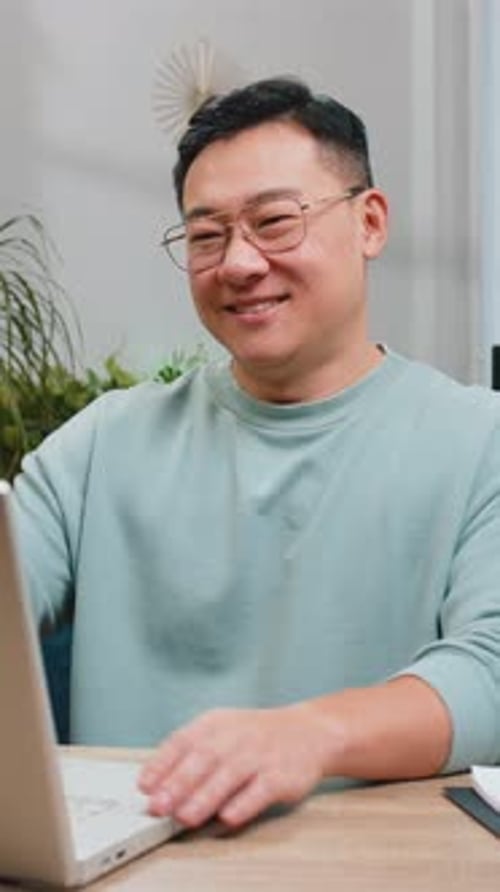 Asiatischer reifer Mann sitzt auf dem Sofa und schließt den Laptop nach Beendigung der Arbeit im Wohnzimmer zu Hause