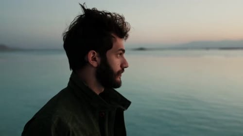 Profilaufnahme eines depressiven Mannes neben einem See bei Sonnenuntergang, der verzweifelt nach oben schaut