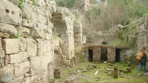 A female traveler with a backpack walks among the ruins of ancient Greek houses, thousands of years.