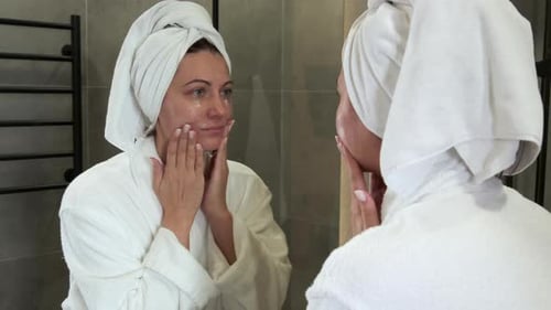 Woman Applying Lotion to Face in Bathroom Mirror